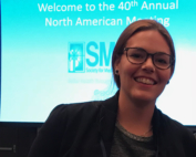 A smiling white woman in front of a conference screen
